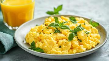 Large portion of scrambled eggs on a plate, placed beside a glass of juice, food photography photo