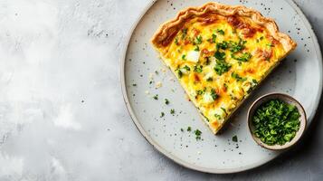 Quiche slice on a plate with a small bowl of garnish beside it, food setting photo