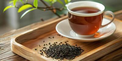 Cup of black tea on a wooden tray with a small pile of tea leaves, food setting photo