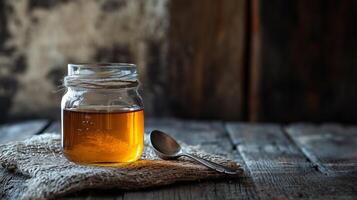 Jar of golden brown syrup with a spoon beside it, placed on a rustic wooden table, meal photography photo