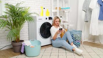 Woman Using Smartphone While Laundry Runs in Modern Apartment video