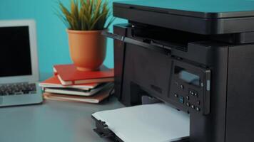 Home office setup with multifunction printer and laptop on desk with potted plant and stacked notebooks for productivity video
