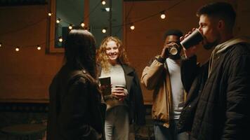 Friends enjoying a late-night gathering outdoors with drinks and string lights during a cozy evening in the city video