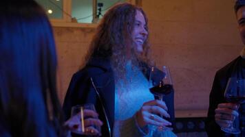 Friends celebrating with wine under twinkling lights in a cozy outdoor setting during a chilly evening video