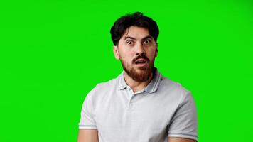 Surprised man makes funny expressions in front of bright green background during home shooting video
