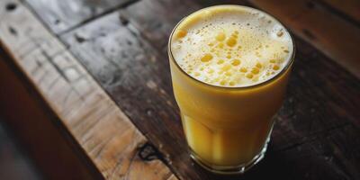 Close-up of frothy yellow beverage in glass cup on dark wooden surface, photorealistic food photo