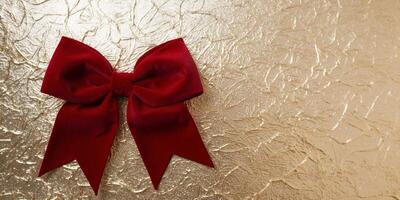Red velvet bow lying on a sparkling gold background with copy space. photo