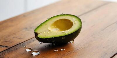 Sliced avocado with water drops on its surface sits on a wooden table. photo