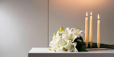 White lilies are laying on a table with burning candles in the background as a symbol of condolences. photo