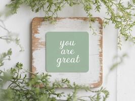 rustic wooden background with small green card with motivational message you are great surrounded by plants decoration copy space. photo
