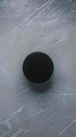 Hockey puck resting on scratched, reflective ice, emphasizing intensity of sport Vertical Mobile Wallpaper photo
