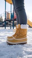 Yellow boots on snow, playground in background suggests crisp winter morning atmosphere Vertical Mobile Wallpaper photo