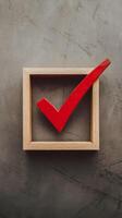 A red checkmark rests in a clean wooden frame on a textured surface Vertical Mobile Wallpaper photo