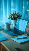 Workspace with laptop, graph, mug, and notebook bathed in blue light Vertical Mobile Wallpaper photo