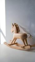 Wooden rocking horse toy sits under soft sunlight against a plain wall Vertical Mobile Wallpaper photo