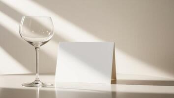 A white card with a blank space sits on a table next to a wine glass. photo