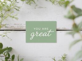 rustic wooden background with small green card with motivational message you are great surrounded by plants decoration copy space. photo