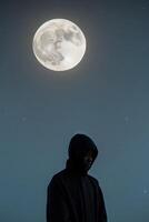 A figure contemplates under a glowing moon. photo