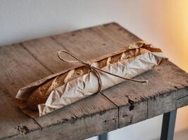 Rustic Baguette Wrapped in Brown Paper on Wooden Table with Warm Ambient Lighting. photo