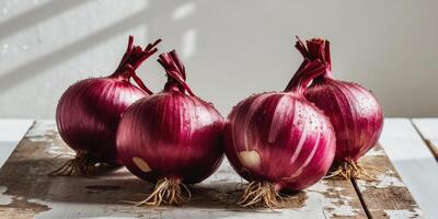 Four whole red onions with roots resting on wooden table. photo