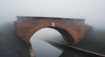 A Tranquil Canal Scene Under a Brick Archway with Mist. photo