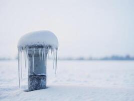 Icy pipe covered in snow and icicles in winter landscape. photo
