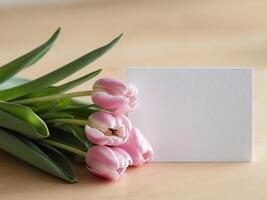 Fresh pink tulips and a blank white card on a light wooden background ideal for greeting messages or invitations. photo