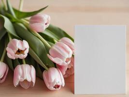 Fresh pink tulips and a blank white card on a light wooden background ideal for greeting messages or invitations. photo