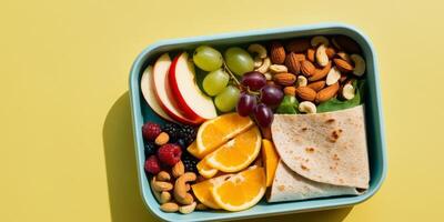 Overhead view of a lunchbox filled with healthy and delicious foods like fresh fruits nuts and a nutritious wrap on a vibrant yellow background. photo
