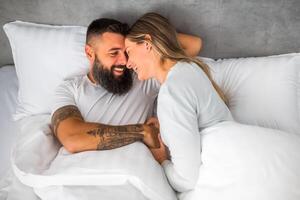 Young happy loving couple is lying in bed in the morning. They are relaxing and smiling. photo