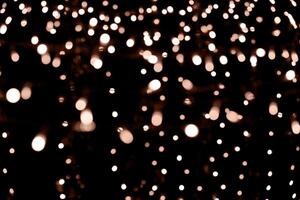 Blurry garland lights on a dark background. Festive Christmas and New Year background. Soft focus. Image toned in color of the year 2024 - Peach Fuzz photo
