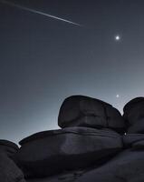 A comet and a rock formation in the night sky photo
