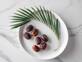 Dates on a white plate with palm leaf on a marble background photo