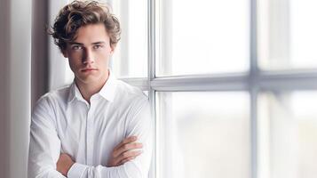 A man in a white shirt standing by a window photo