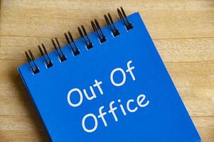 Top view of Out Of Office text on blue notepad on wooden desk. Away from work concept photo