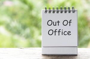 Out Of Office text on white notepad with blurred nature background photo