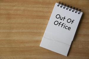 Top view of Out Of Office text on white notepad on wooden desk. Away from work concept photo