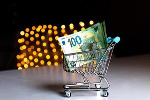 Christmas shopping online.Trolley with 100 euro notes on background of blurred bokeh lights photo