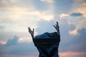 Human hands in a black plastic bag on a sunset sky background photo