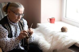old woman knitting in a home by the window photo