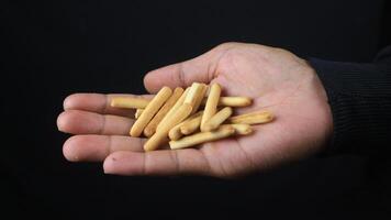hand holding crispy straw biscuit sticks on black background. photo