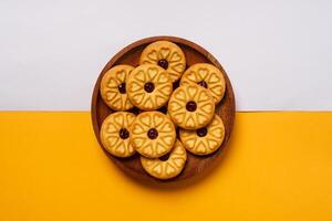 Strawberry jam biscuits on a wooden plate, decorated with a circular heart motif on their surface, isolated on white and orange background. High resolution photo. photo