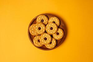 Strawberry jam biscuits on a wooden plate, decorated with a circular heart motif on their surface, isolated on orange background. High resolution photo. photo
