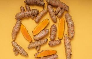 Fresh turmeric root and slices isolated on yellow background. High resolution photo. photo