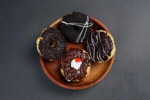 Donuts with different types of topping served on wooden plate, top view on black background. High resolution photo. photo
