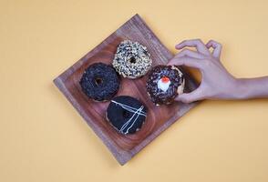 Donuts with different types of topping served on wooden plate, top view on yellow background. High resolution photo. photo