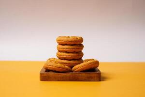 Pile of strawberry jam biscuits on a wooden plate, decorated with a circular heart motif on their surface, isolated on white and orange background. High resolution photo. photo