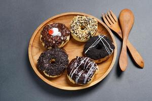 Donuts with different types of topping served on wooden plate, top view on black background. High resolution photo. photo
