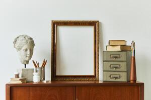 Stylish composition of artist workspace room with design retro teak commode, mock up poster frame, book, decoration and painting accessories. Template. photo