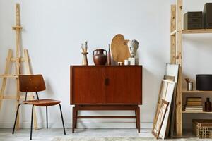 Stylish composition of artist workspace with design retro teak commode, chair, bookcase, poster frames, easel, decoration and elegant personal accessories. Template. photo